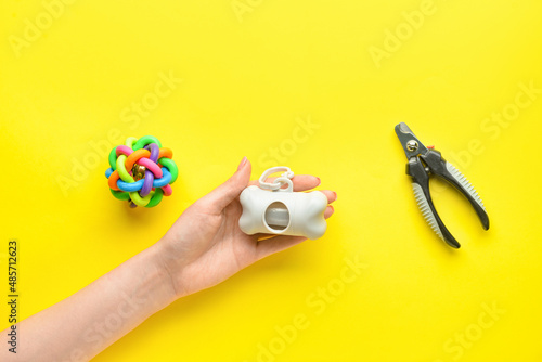 Female hand with pet waste bags, nail clipper and toy on yellow background