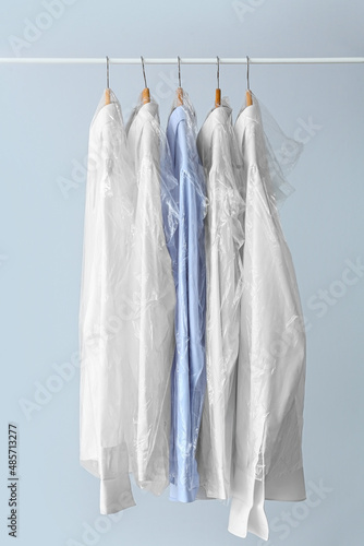 Rack with clean shirts in plastic bags on grey background