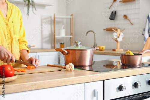 Cookware and woman slicing carrots on wooden board in kitchen