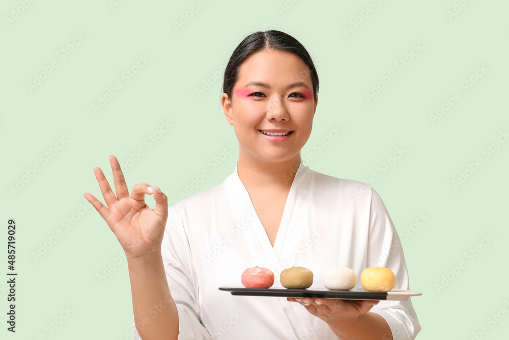 Beautiful Asian woman with tasty Japanese mochi showing OK on color background Beautiful Asian woman with tasty Japanese mochi showing OK on color background