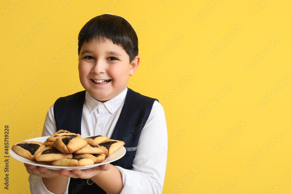 Little Jewish boy with tasty Hamantaschen for Purim holiday on color background Little Jewish boy with tasty Hamantaschen for Purim holiday on color background