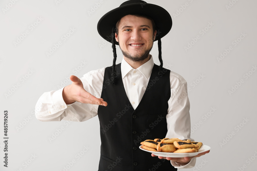 Young Jewish man with tasty Hamantaschen for Purim holiday on grey background Young Jewish man with tasty Hamantaschen for Purim holiday on grey background