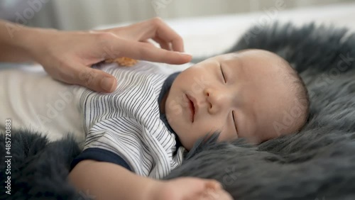 Close-up of a newborn, 2 month old Asian, sleeping on a gray carpet with his mother warmly watching over him. and a mother's hand touched the little boy's cheek