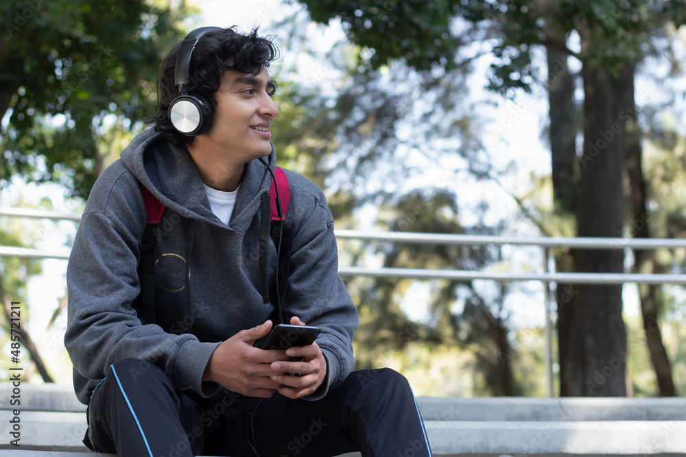 Obraz premium young man enjoying some time alone relaxing listening to music with his headphones in the park, he has a smile on his face and a facial expression of peace and well-being.