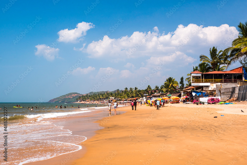 Tourists at tropical, sandy Anjuna Beach on the Goa coast with blue sky, India