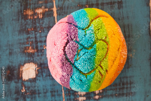 Colorful Rainbow Concha Mexican Pastry on a blue wooden table. A sweet bread with a Heart Shape for LGBT Valentines - a symbol of queer love.