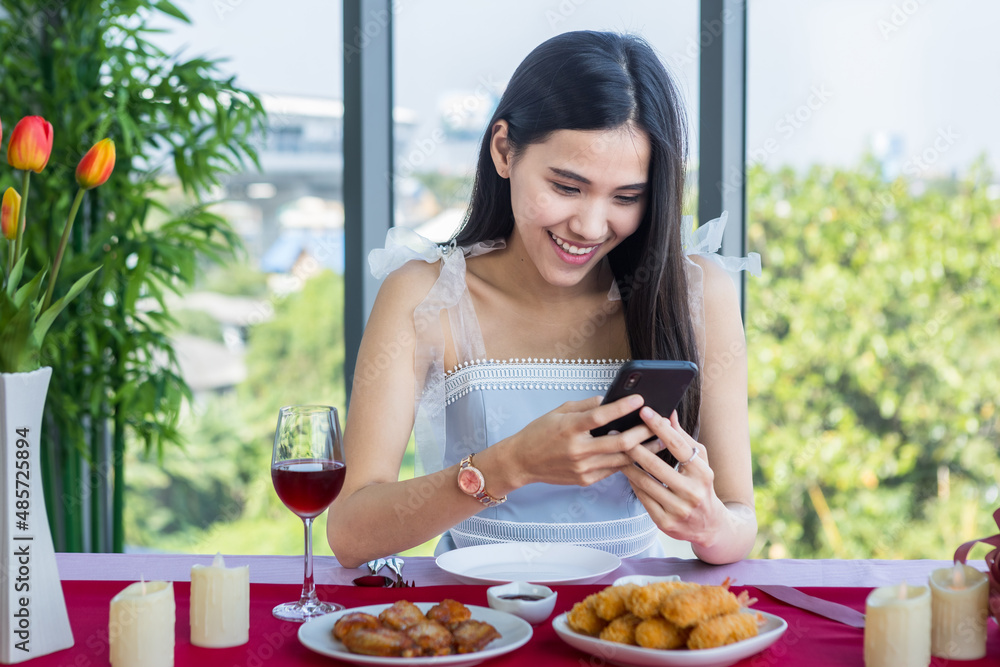 Valentine's day concept,happy asian young female talking on smartphone sitting at a table food with wine glasses and bouquet of red and pink roses at in the restaurant background