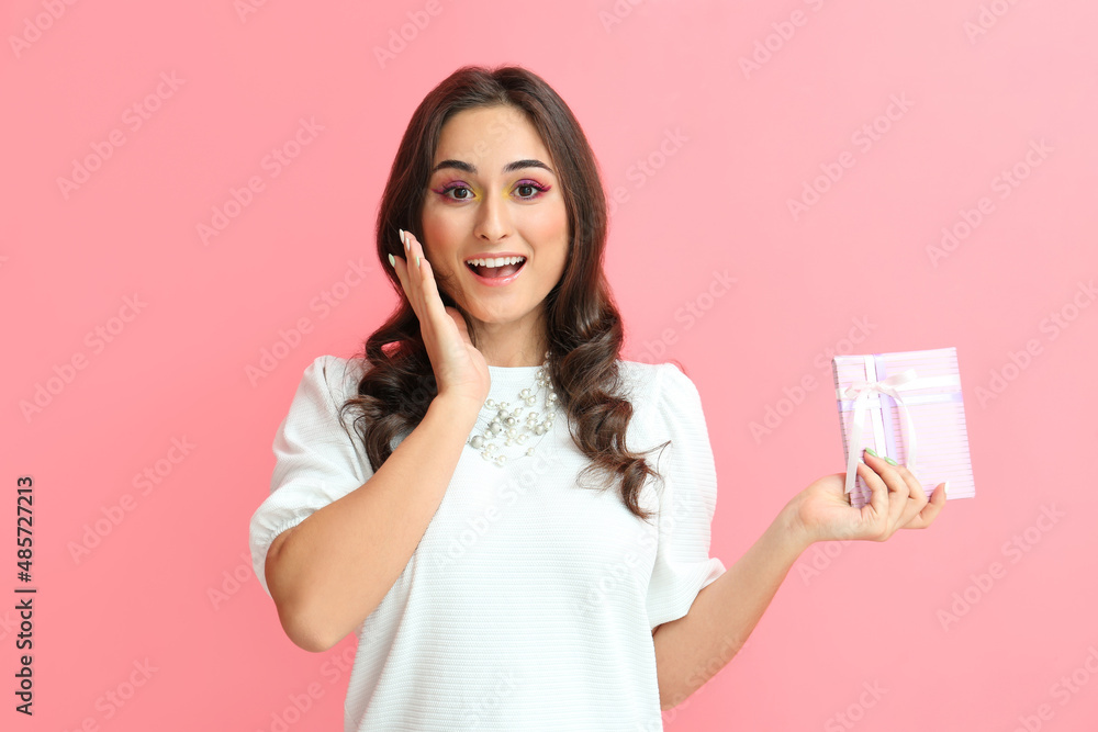 Emotional woman with creative makeup holding gift box on pink background. International Women's Day Emotional woman with creative makeup holding gift box on pink background. International Women's Day