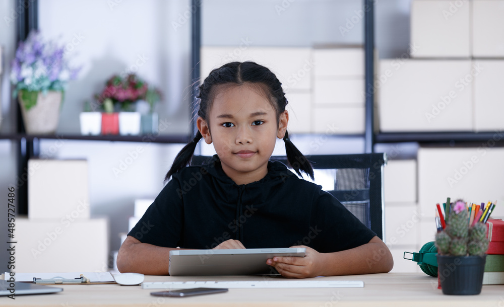 Portrait shot of Asian young cute happy primary schoolgirl in casual outfit sitting at working table holding tablet computer in hands for advertising copy space and text Portrait shot of Asian young cute happy primary schoolgirl in casual outfit sitting at working table holding tablet computer in hands for advertising copy space and text