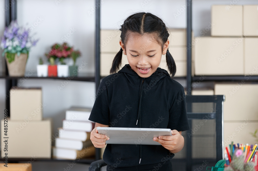 Portrait shot of Asian young primary schoolgirl in casual outfit standing smiling holding showing tablet computer in hands for advertising copy space and text Portrait shot of Asian young primary schoolgirl in casual outfit standing smiling holding showing tablet computer in hands for advertising copy space and text