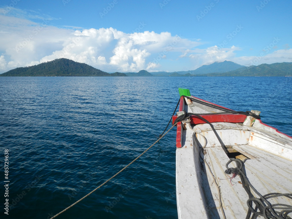 Wooden ship sailing on blue sea with island and blue sky background