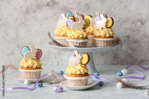 Stand with tasty Easter cupcakes and eggs on light background