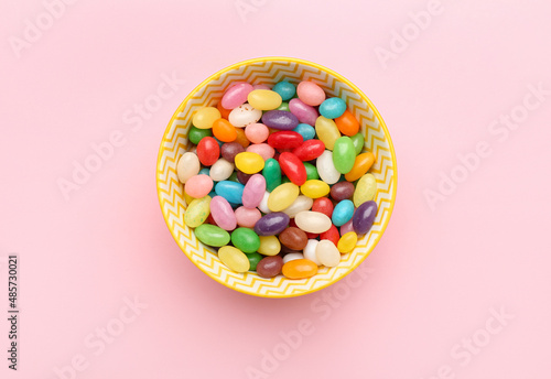 Bowl with multicolored jelly beans on color background
