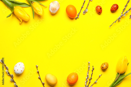 Beautiful Easter eggs, willow branches and tulip flowers on yellow background
