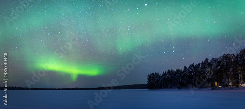 Northern Lights (aurora borealis) over a snow covered icy frozen lake in winter in Finnish Lapland, inside Arctic Circle in Finland