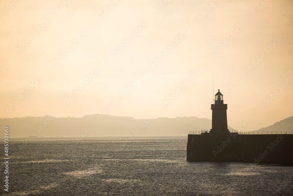 Lighthouse in St Peter Port Harbour at sunrise, Guernsey, Channel Islands, United Kingdom, seascape background with copy space