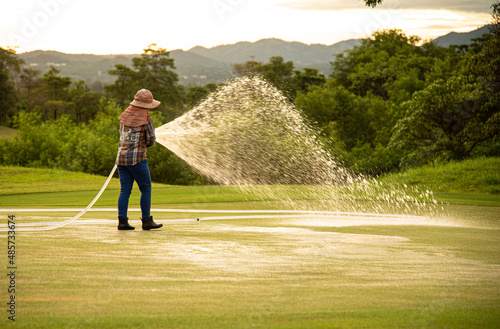 worker watering golf green in morning sunlight