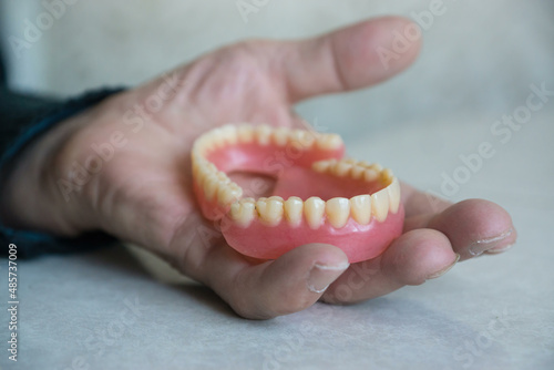 Close-up of a pensioner's hand holding a false teeth in his hand. Removable dentures in a man's hand. Implantation, dental treatment topic. selective focus