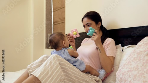 An attractive lady sitting with a cute girl child on her lap at home - baby sitting. A young Indian mother and her pretty little daughter playing with toys - parenting  emotional bonding  nuturing photo