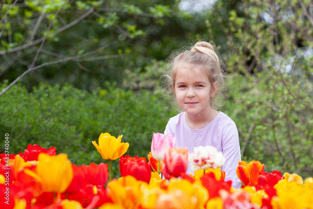 A beautiful pretty girl sits near a flower bed of tulips. A beautiful pretty girl sits near a flower bed of tulips.