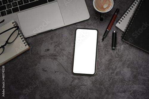 Mockup smart phone, laptop computer, notebook and coffee cup on dark stone textured table.