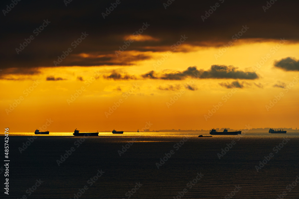 silhouettes of ships at sea against a bright sunset sky, sunlight reflected from the waves, dramatic sky