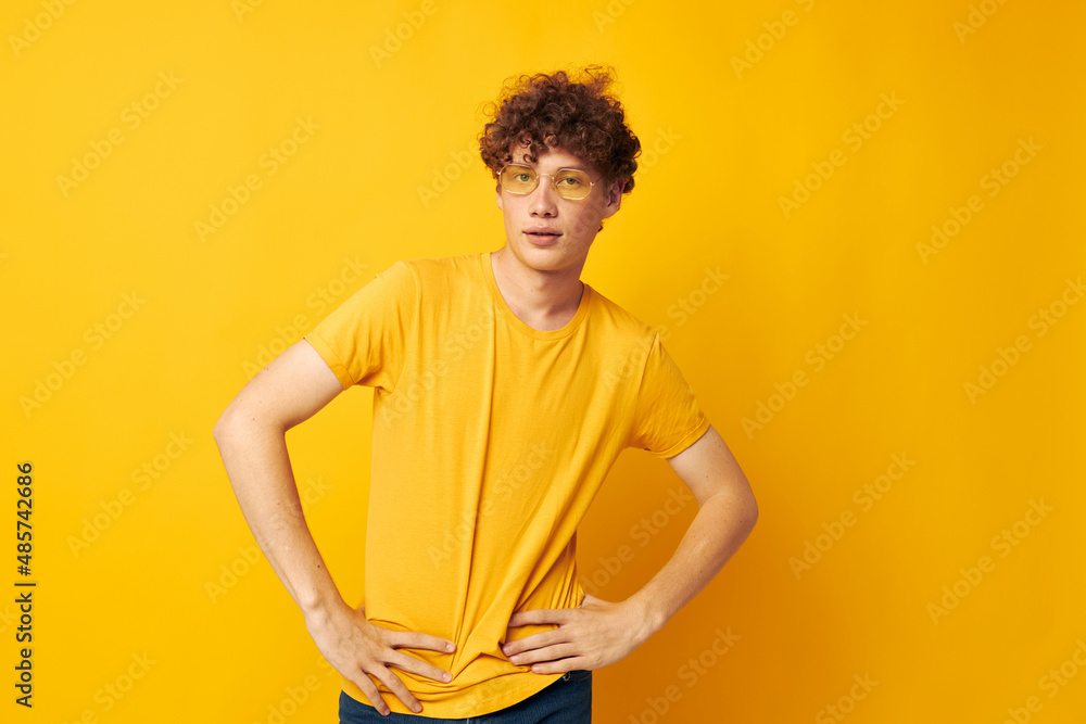 portrait of a young curly man wearing stylish glasses yellow t-shirt posing yellow background unaltered portrait of a young curly man wearing stylish glasses yellow t-shirt posing yellow background unaltered