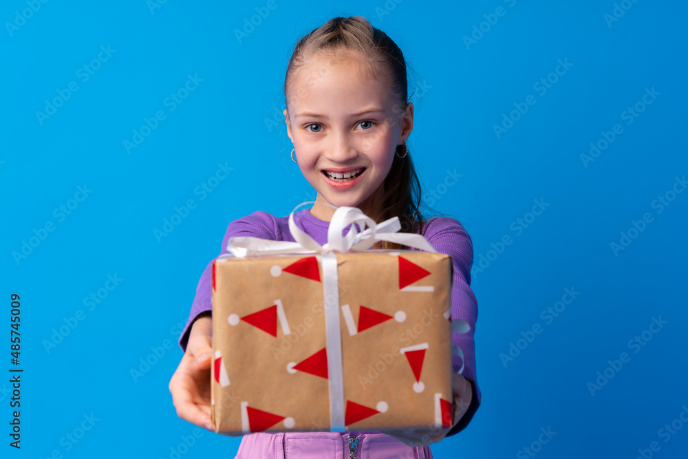 Happy little girl with long hair holding a gift box on a blue background Happy little girl with long hair holding a gift box on a blue background