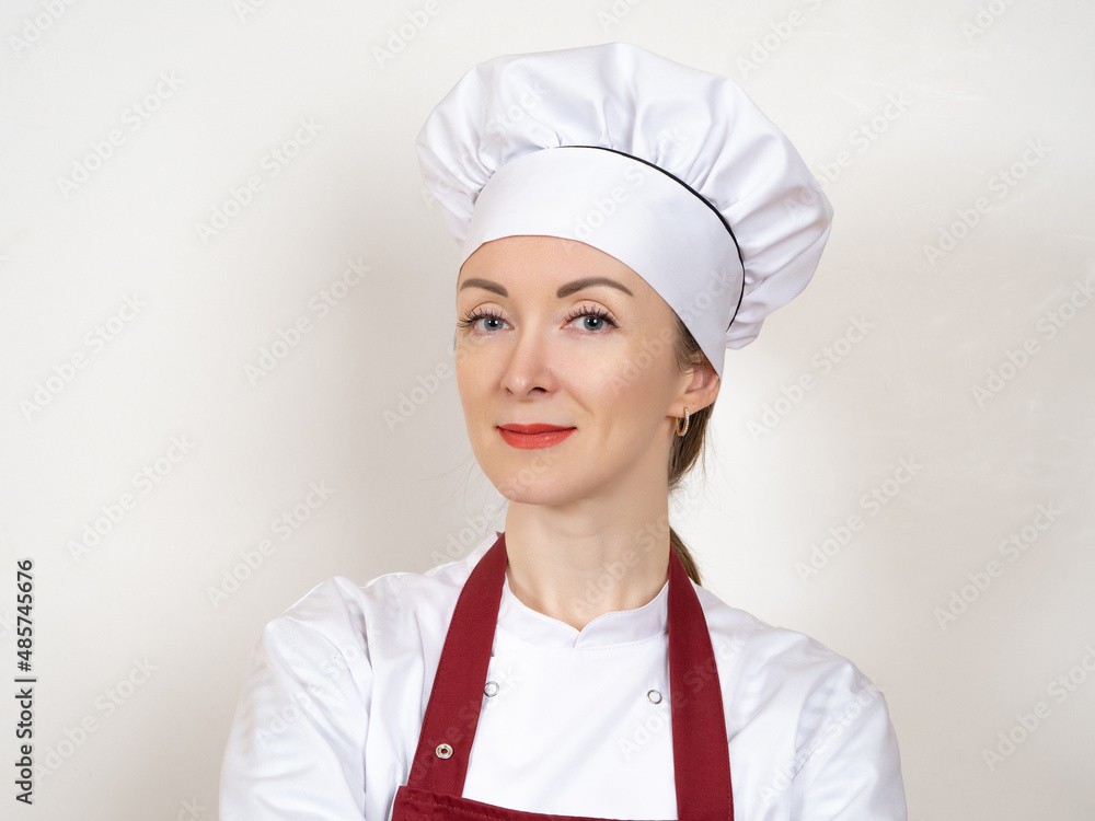 Cook woman. Close-up portrait of girl cook. Woman cook on light background. Woman in white chef's hat. Successful chef is looking at camera. Career as professional chef. Restaurant worker Cook woman. Close-up portrait of girl cook. Woman cook on light background. Woman in white chef's hat. Successful chef is looking at camera. Career as professional chef. Restaurant worker