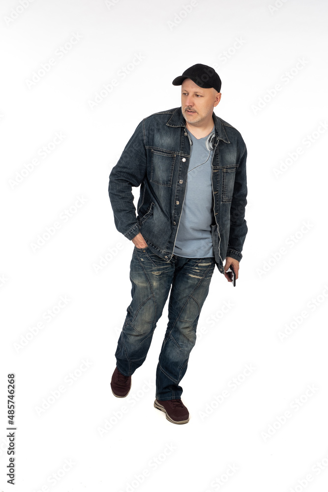 Man on white. Portrait of man with mobile phone in his hands. Guy is walking in denim casual clothes. Human walks and keeps his hand in his pocket. Walking adult male isolated. Guy in cap. Man on white. Portrait of man with mobile phone in his hands. Guy is walking in denim casual clothes. Human walks and keeps his hand in his pocket. Walking adult male isolated. Guy in cap.
