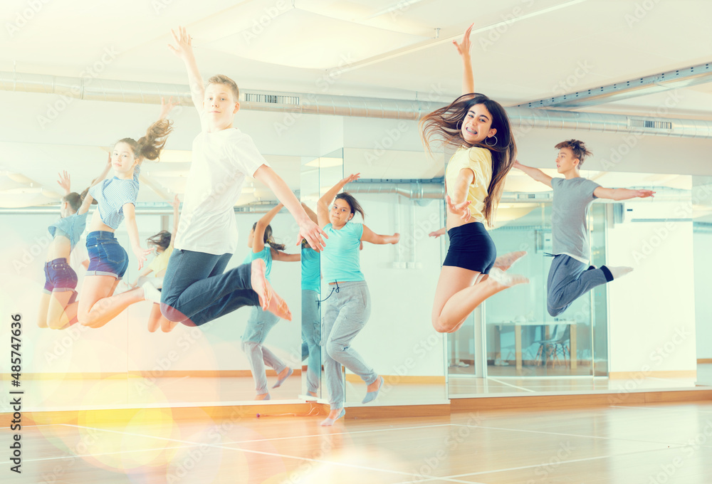 Group of cheerful teenagers dancing and jumping in dance studio during class, side view