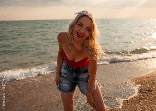 Beautiful strong woman with short hair wearing red swimming suit and shorts walking in the beach against the blue sky and sea