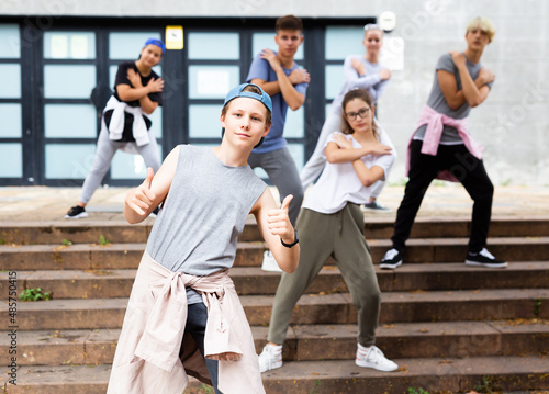 Confident teenager street dancer posing during performance with group in summer city .