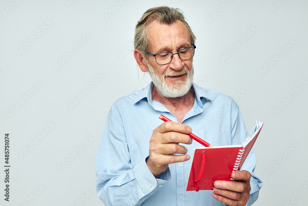 Senior grey-haired man with red notebook and pen light background Senior grey-haired man with red notebook and pen light background
