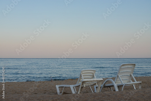 Two sunbeds on a sandy calm beach with turquoise sea water and white sand © Oleh Marchak