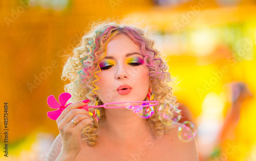 Happy girl with colorful summer rainbow makeup inflates soap bubbles. Emotions of happiness and fun. Summer vacation, playful mood at the party, funny soap bubbles.