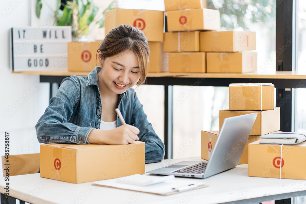 Young business start up online seller owner using computer for checking the customer orders from email or website and preparing packages for product office equipment. Young business start up online seller owner using computer for checking the customer orders from email or website and preparing packages for product office equipment.