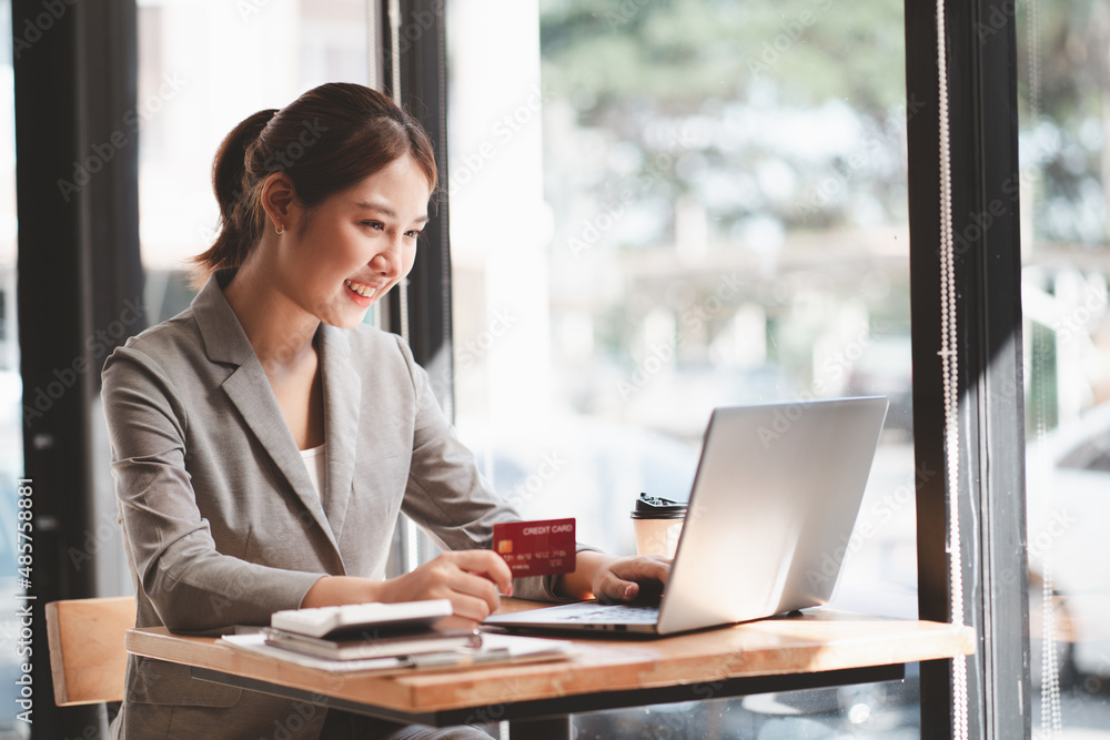 Young woman holding credit card and using laptop computer. Businesswoman working at home. Online shopping, e-commerce, internet banking, spending money, working from home concept Young woman holding credit card and using laptop computer. Businesswoman working at home. Online shopping, e-commerce, internet banking, spending money, working from home concept