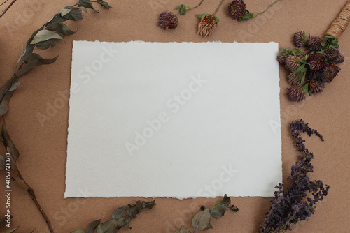 Blank paper mockup of watercolor paper with dry herbs on table against craft paper background 