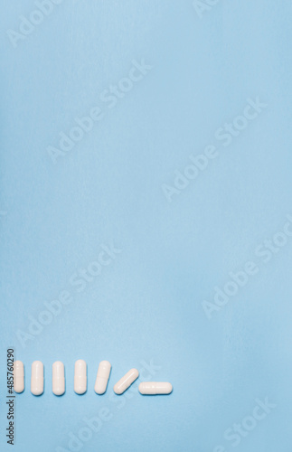 Vertical banner white tablets or capsules lie on a light blue background and gradually fall with space for text. Useless pharmaceutical  Covid-19 or coronavirus