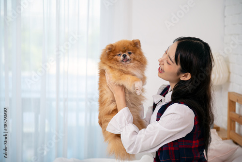 Young pretty Asian woman sitting and embracing Brown Pommeranian dog on white bed with copy space. photo