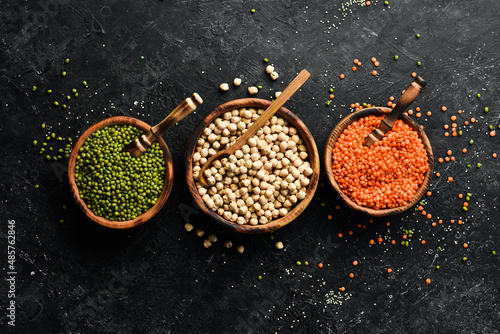 Set of organic cereals in bowls: chickpeas, mung beans, lentils. Healthy food. On a black stone background.