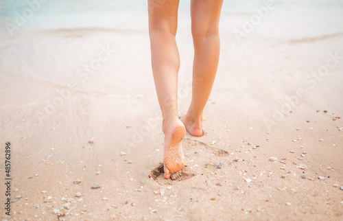 Female legs walking along the seaside barefoot, close-up of the perfect tanned legs of a girl coming out of the water after swimming. Woman relaxing on vacation, enjoying time at the beach