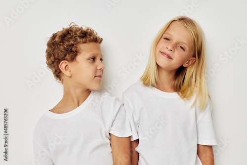 Portrait of cute children in white T-shirts are standing next to beige background