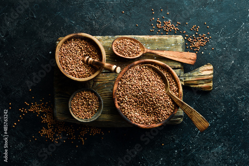 Organic buckwheat groats in a wooden spoon on a stone background. Top view.