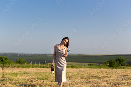 Young girl on the field with a bottle in her hands. Summer season sunset.