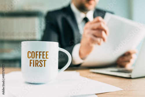 Coffee first quote on white mug in business office, businessman reading financial report in the back © Bits and Splits