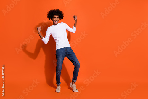 Photo of excited lucky guy wear white shirt rising fists empty space isolated orange color background © deagreez