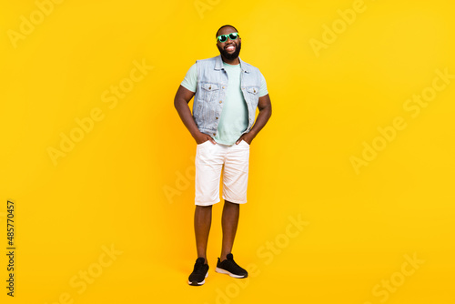 Full length body size view of attractive cheery guy hipster holding hands in pockets isolated over bright yellow color background