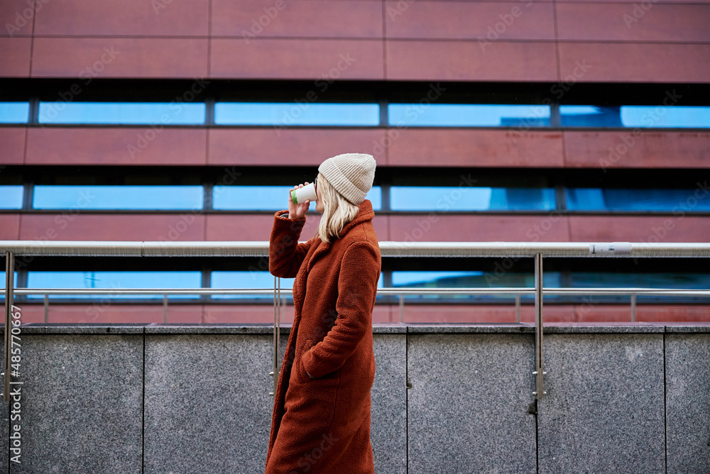 Young woman in eyeglasses wearing coat walking at city street with cup of coffee takeaway Young woman in eyeglasses wearing coat walking at city street with cup of coffee takeaway
